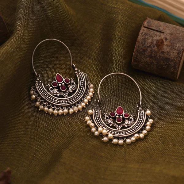 Saara red stone oxidised hoop earrings with peacock motifs and faux pearl drops on olive fabric